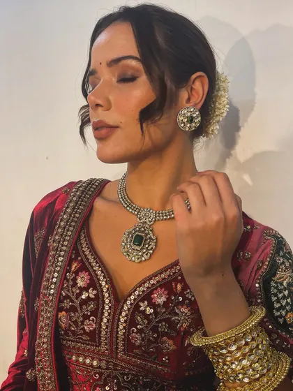 This image highlights the perfect pairing of a rich velvet lehenga with an emerald and polki diamond necklace. Coordinating the jewellery with the outfit's tones is key to a harmonious bridal look.