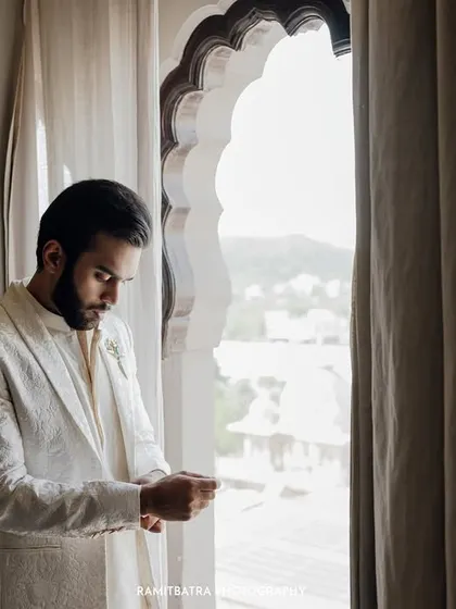A groom adjusts his cuffs by an arched window at Fairmont Jaipur, a classic, pensive portrait before the ceremony.