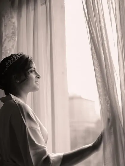 The bride in her robe, looking out the window, with her wedding dress hanging in the background. A moment of quiet anticipation.