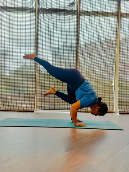A moment of focus in Eka Pada Bakasana (One-Legged Crow). This advanced arm balance requires a strong core and precise control to lift one leg up and away.