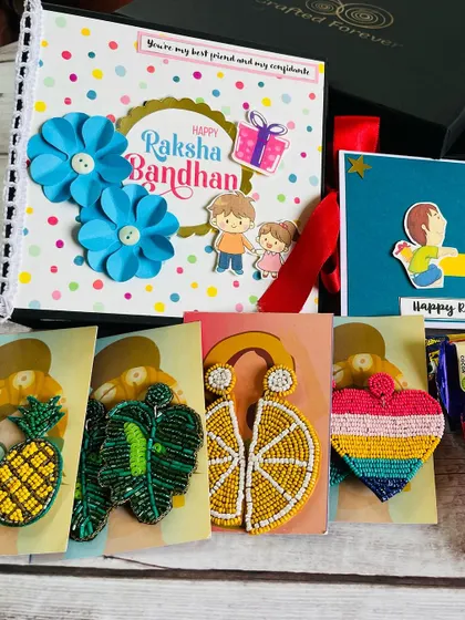 Here is a closer look at our Rakhi hamper for a sister. It includes a custom album, a greeting card, and a selection of our colorful, handmade beaded earrings to choose from.