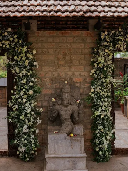 Stone pillars adorned with cascading white floral arrangements, framing a deity statue.