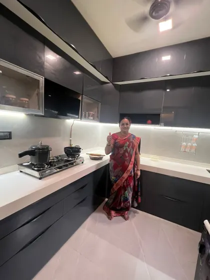 A happy client giving a thumbs-up in her brand new dark grey modular kitchen. The high-gloss acrylic finish and handleless design create a super modern and sophisticated look.