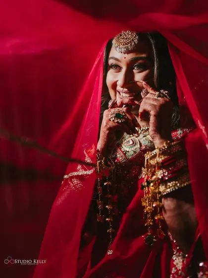 A classic shot of the bride peeking through her red veil, her smile full of happiness and mischief.
