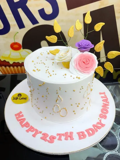 A delicate 2.5kg white cake for a 25th birthday, adorned with sugar flowers and gold leaf accents.