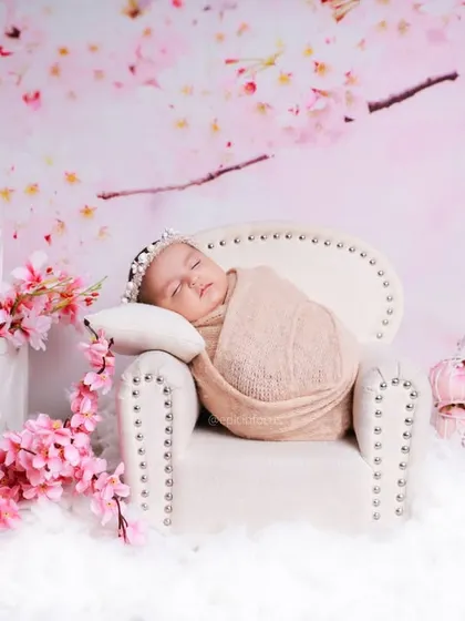 Even though the block says 'ONE', this image showcases a newborn-style pose. A peacefully sleeping baby is swaddled and placed on a miniature couch amidst a dreamy cherry blossom theme.