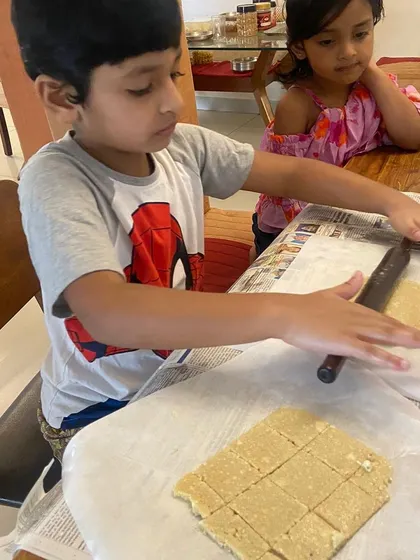 A sibling watches as her brother engages in a cookery activity. Learning at home provides wonderful opportunities for family involvement and for older children to model concentration and skill.