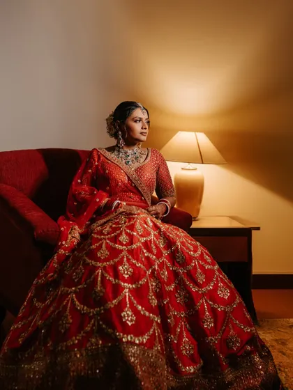 A classic bridal portrait of a Sabyasachi bride. The warm lighting and her regal pose in the stunning red lehenga create an image of timeless elegance.