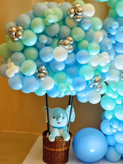 A close-up of a hot air balloon prop made of blue and green balloons, with a cute stuffed elephant ready for an adventure.