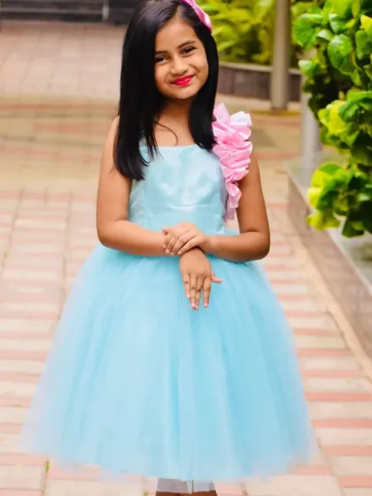 A full-length view of the custom sky blue frock with a unique pink floral arrangement on the shoulder.