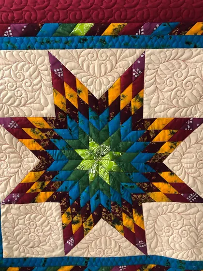 A close-up of a "Glowing Star" quilt, showing the intricate feather quilting in the background.