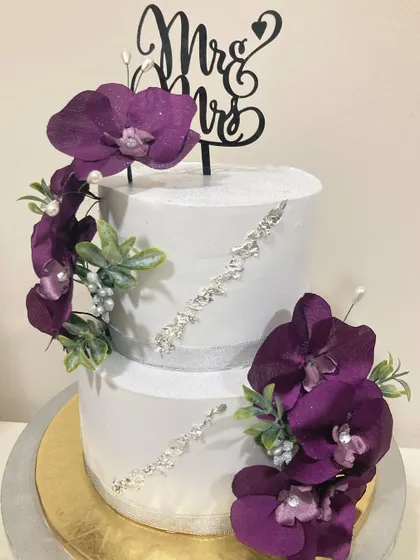 A modern and luxurious two-tier wedding cake. The design features striking purple orchids and a fault line of edible silver crystals for a touch of glamour.