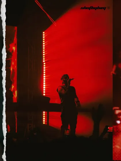 A wide shot of Talwiinder on stage, silhouetted against a massive red-lit screen. This image emphasizes the scale of the production and his solitary presence.