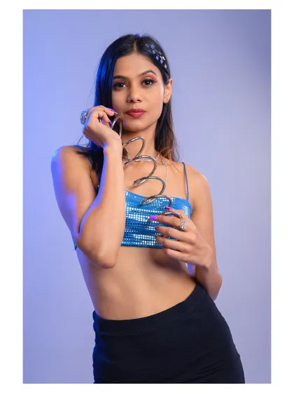 A vibrant studio portrait with cool-toned lighting. The sequined top and playful pose create a fun and modern look, perfect for a party or event-themed shoot.
