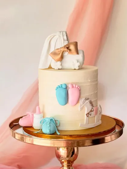 A sweet gender reveal cake with pink and blue baby feet. The cake is decorated with a baby bassinet topper, a rocking horse, and other baby-themed items.