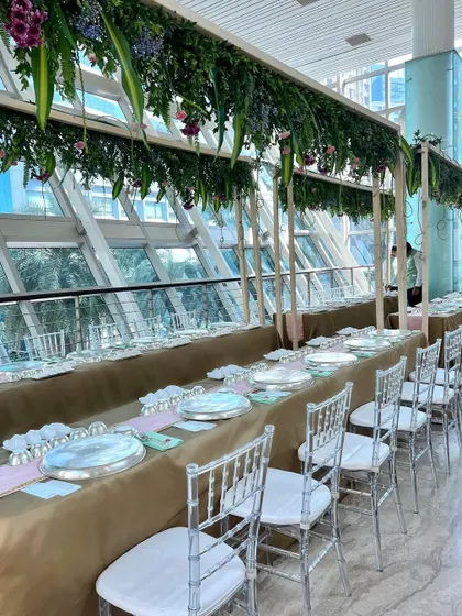A sit-down Indian style thali lunch with contemporary decor, featuring a long table setting under a canopy of hanging greenery.