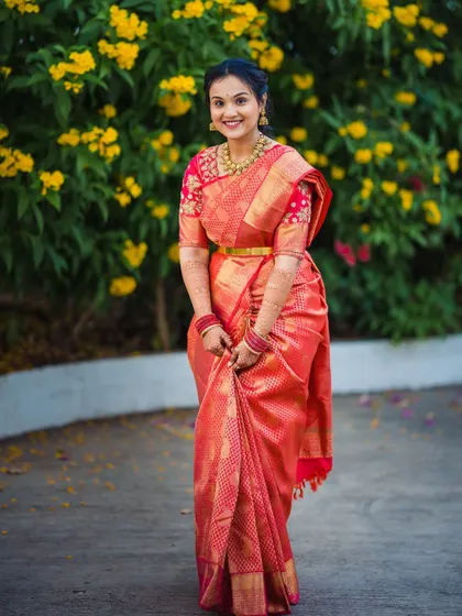 A full-length portrait of the bride, Devika, showcasing her stunning red and gold engagement saree.