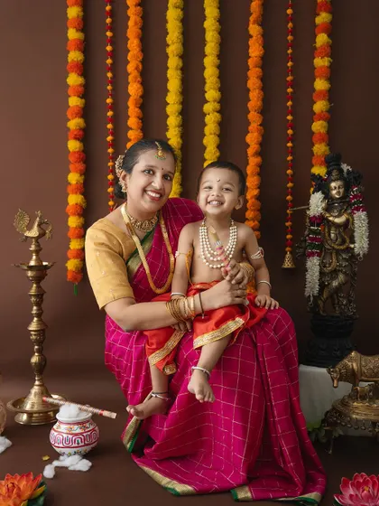 A happy, full-length portrait of a mother and son celebrating Janmashtami with traditional decor.