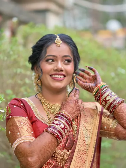 A happy, smiling portrait of the bride adjusting her earring. The shot highlights her intricate jewelry and flawless makeup.