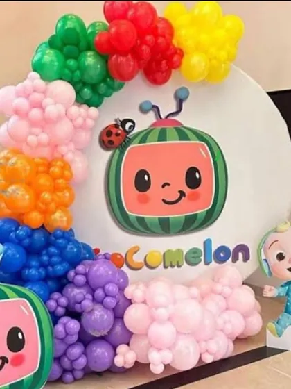 A close-up of a Cocomelon themed decoration. This features a custom backdrop with the Cocomelon TV character, framed by a rainbow of balloons, and includes a small JJ character cutout.