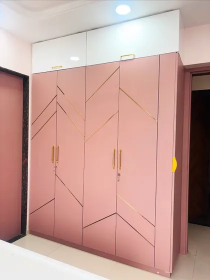 A four-door hinged wardrobe in a lovely matte pink finish with gold metal strips creating an abstract geometric design.