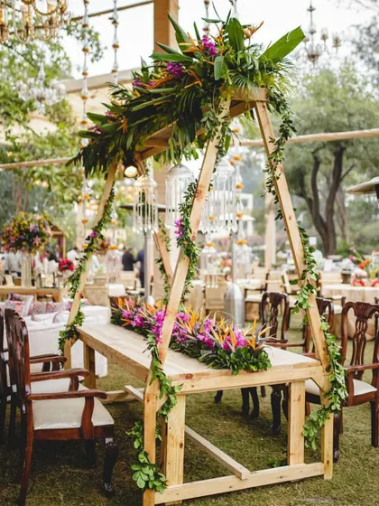 A unique dining table setup with a wooden A-frame structure overhead, adorned with tropical flowers and greenery. This created an intimate and beautifully framed dining experience for the head table.