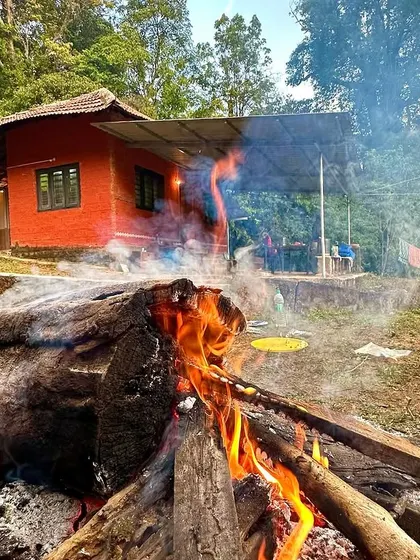 A large log bonfire smolders at a rustic jungle homestay in Agumbe. This is the heart of the campsite, where teams gather for warmth and stories.