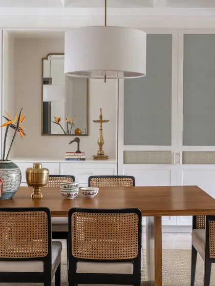 A close-up of the dining space, highlighting the classic symmetry, warm wood table, and monochrome chairs with cane backing. Brass accents in the lighting and decor add a touch of warmth and elegance.