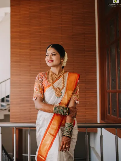 An off-white Kanjeevaram provides a beautiful canvas for a pop of color. This bride’s saree with its bright orange border is paired with a matching blouse that features detailed embroidery, perfect for a daytime wedding.