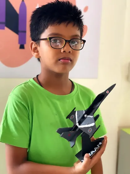 A student proudly holds up the detailed fighter jet model he assembled and painted.