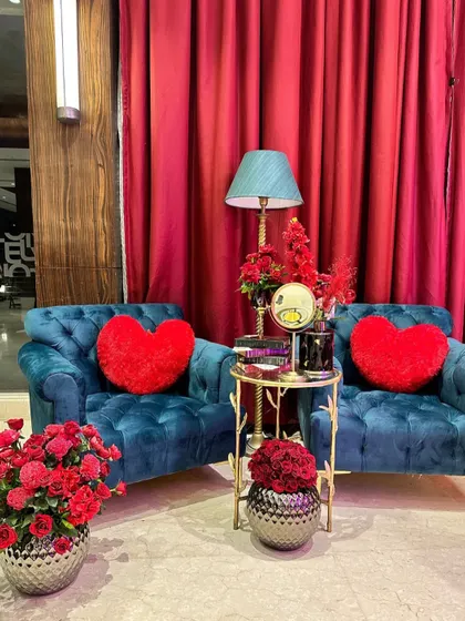 A romantic seating arrangement with two blue armchairs, red heart-shaped cushions, and vases of red roses, creating an intimate corner for two.