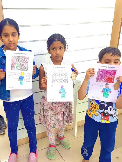 Mission accomplished! Three young participants hold up their completed maze worksheets, a fun and educational activity that complements our hands-on building challenges.