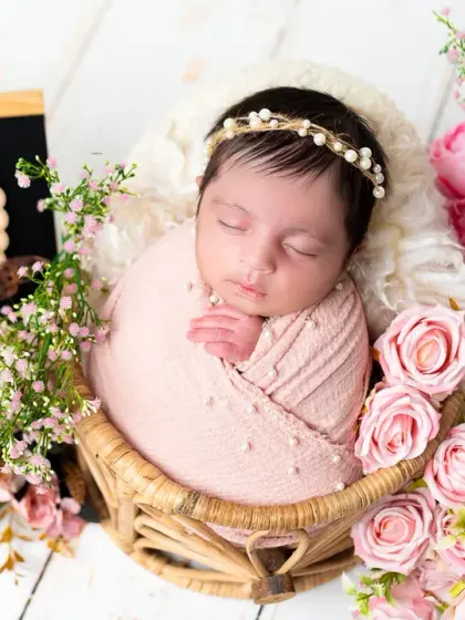 A classic newborn portrait, with the baby swaddled in pink and nestled in a basket of flowers. This timeless style focuses on the simple beauty of your new arrival.