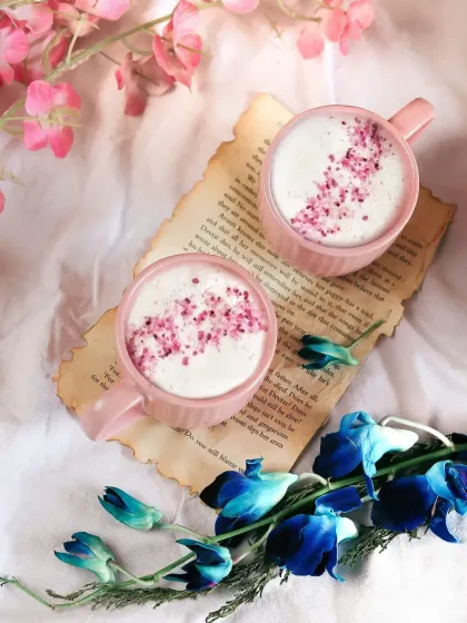 Two pink mugs of coffee topped with floral sprinkles, styled on a vintage book page. This whimsical and romantic flatlay is perfect for a cafe with a unique, aesthetic vibe.