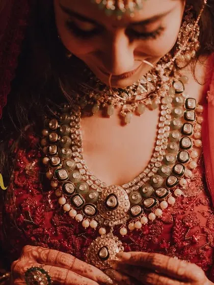 A close-up on the bride's stunning necklace and the intricate details of her red bridal blouse. This shot highlights the beauty of her wedding jewelry.