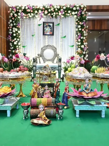 A classic South Indian Seemantham setup. The decor features an elegant floral arch, a traditional silver chair for the mother-to-be, and an elaborate display of fruits and sweets on decorated plates.