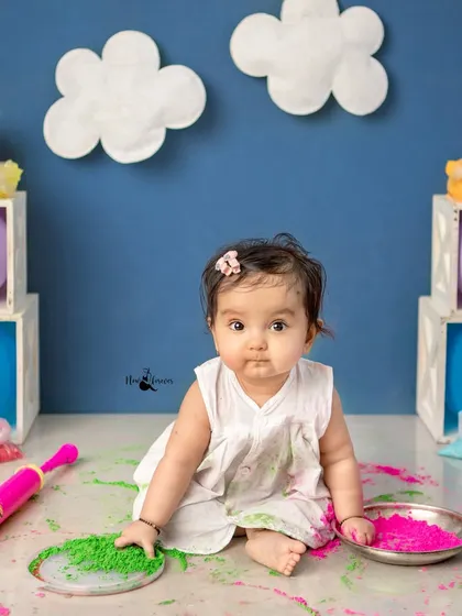 A younger baby getting her first taste of Holi with safe green and pink colors.