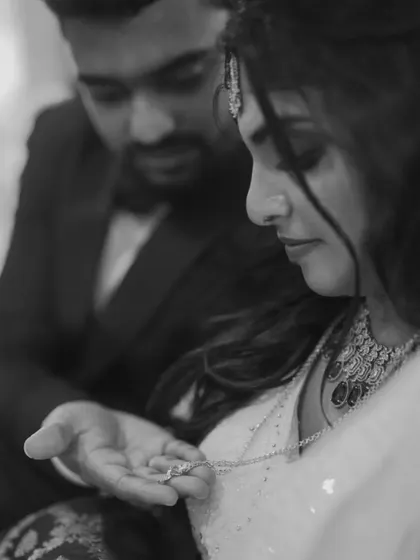 A dramatic black and white shot of a groom presenting a necklace to his bride, highlighting the emotion and the jewelry.