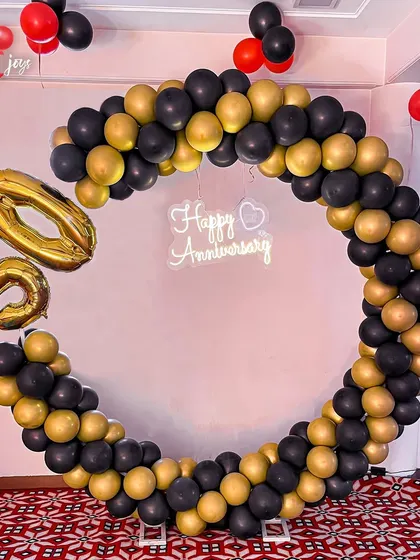 Celebrating 50 golden years together! A chic and modern circular balloon arch in black and gold, with large '50' foil balloons and a 'Happy Anniversary' neon sign, marks this incredible milestone in style.