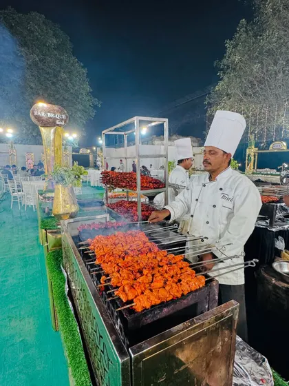 A chef grilling chicken tikka skewers at a live station, with racks of other kebabs ready for serving.
