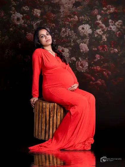A powerful and artistic portrait of a mom-to-be in a red gown. The dark floral backdrop and water reflection effect create a moody and dramatic look.