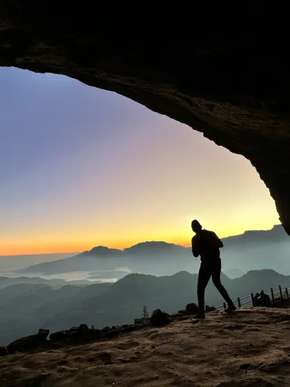 A trekker silhouetted against the sunrise, seen from inside a cave at Ratangad. These are the moments of quiet reflection that make hiking so special.