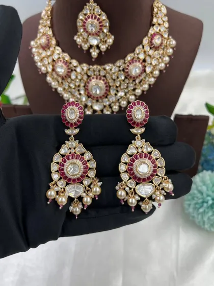 The Zarista Premium Moissanite Necklace set, shown here in both ruby and green variations. This set includes a necklace, maang tikka, and earrings, featuring large central stones surrounded by detailed craftsmanship.