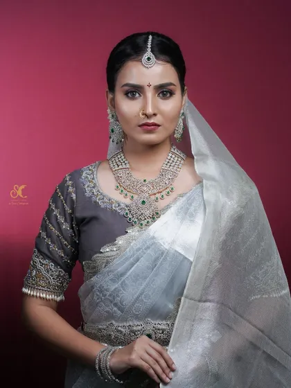 A stunning studio portrait for a makeup artist's portfolio, showcasing a 'Muhurtham' bridal look. The clean background and professional lighting emphasize the intricate details of the makeup and jewelry.