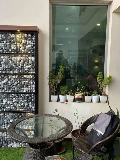 This cozy seating nook on the balcony is set against a unique gabion wall filled with river stones. This feature adds a modern, textural element to the design, complemented by potted plants for a touch of green.