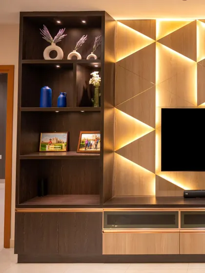 The geometric backlit TV wall is complemented by smart spotlights in the shelving unit, allowing the client to highlight their favorite decor items.