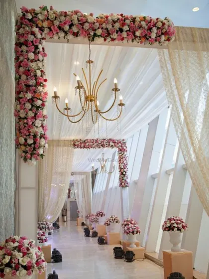 An elegant indoor passage decorated with white drapes and stunning pink and white floral arrangements. The chandeliers cast a warm glow, creating a sophisticated and romantic walkway for guests.