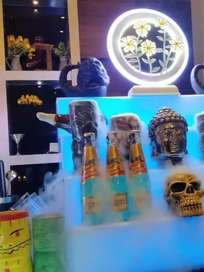 A quirky and themed bar setup featuring unique skull and tiki-style mugs, neon signs, and a smoky effect for a memorable cocktail experience.