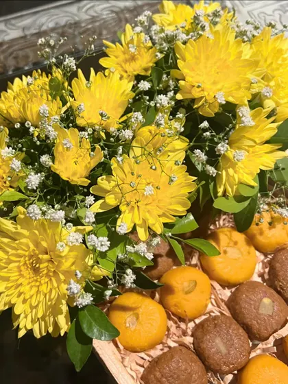Introducing our festive sweet tray, perfect for Haldi or Diwali. This wooden tray is filled with traditional Indian sweets like peda and ladoo, arranged alongside a bright bouquet of yellow chrysanthemums.