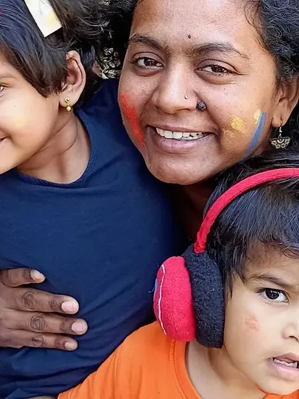 A teacher and children with faces smudged with color, sharing a happy moment during Holi. We celebrate this festival of colors with laughter, joy, and togetherness.